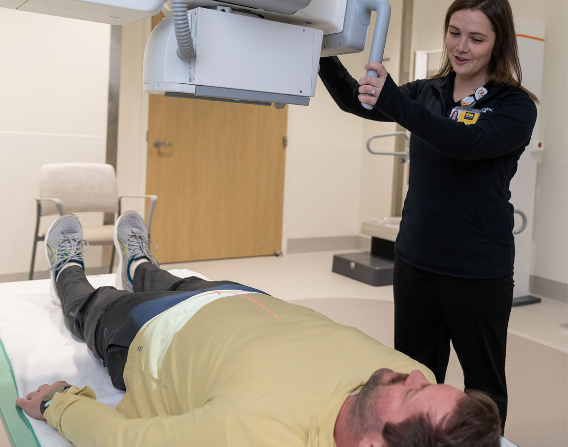 Rad tech positioning an x-ray scanner over patient laying on a table