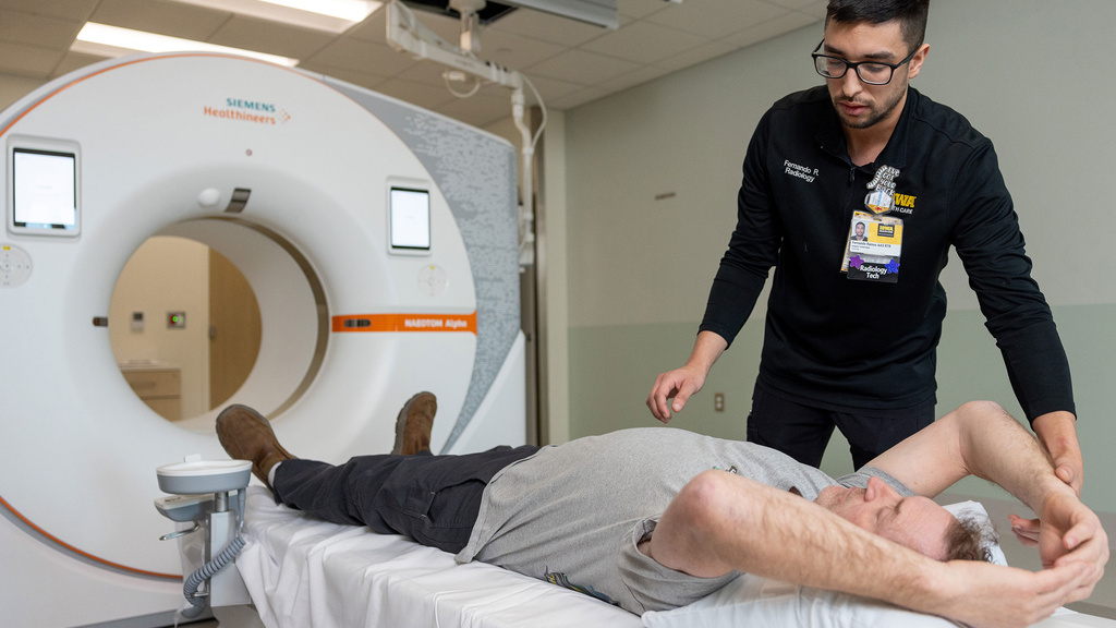 Rad tech positions patient lying on a table in front of a CT scanner