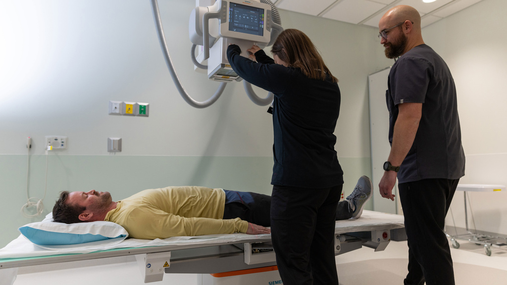 Two rad techs positioning an x-ray above a patient lying on a table